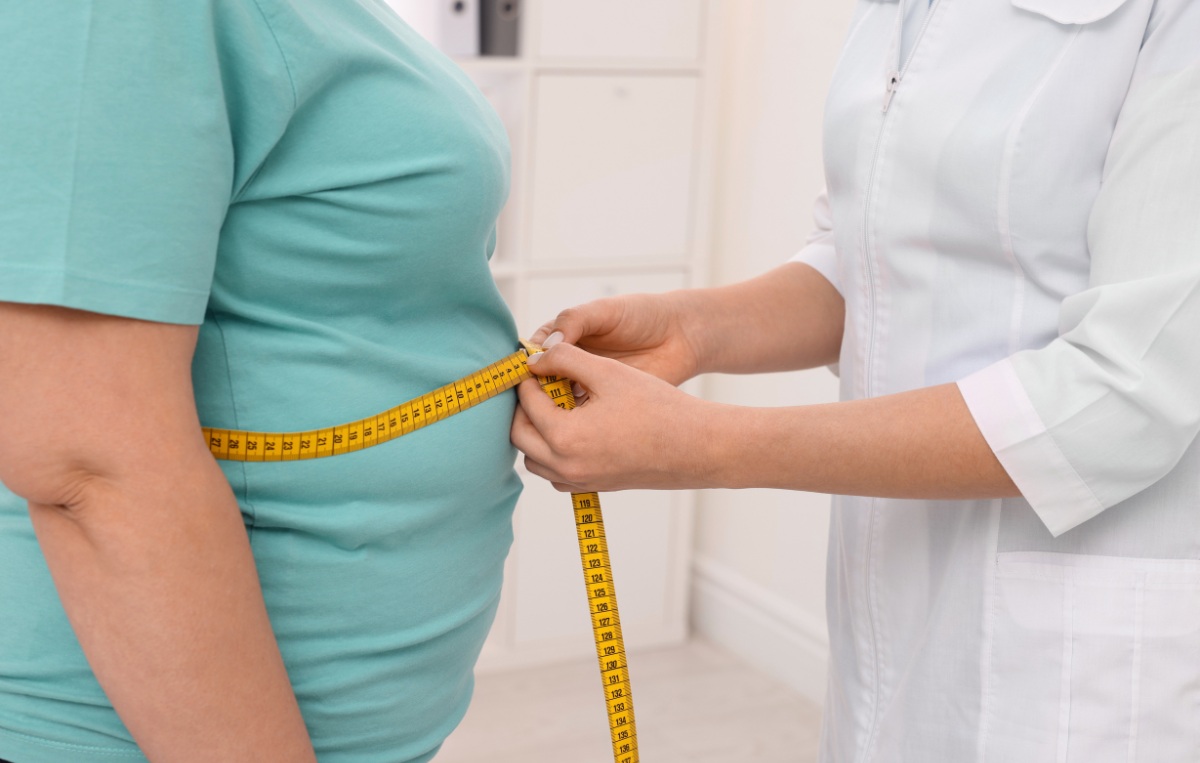 a medical professional in a white lab coat measuring a patient's waist