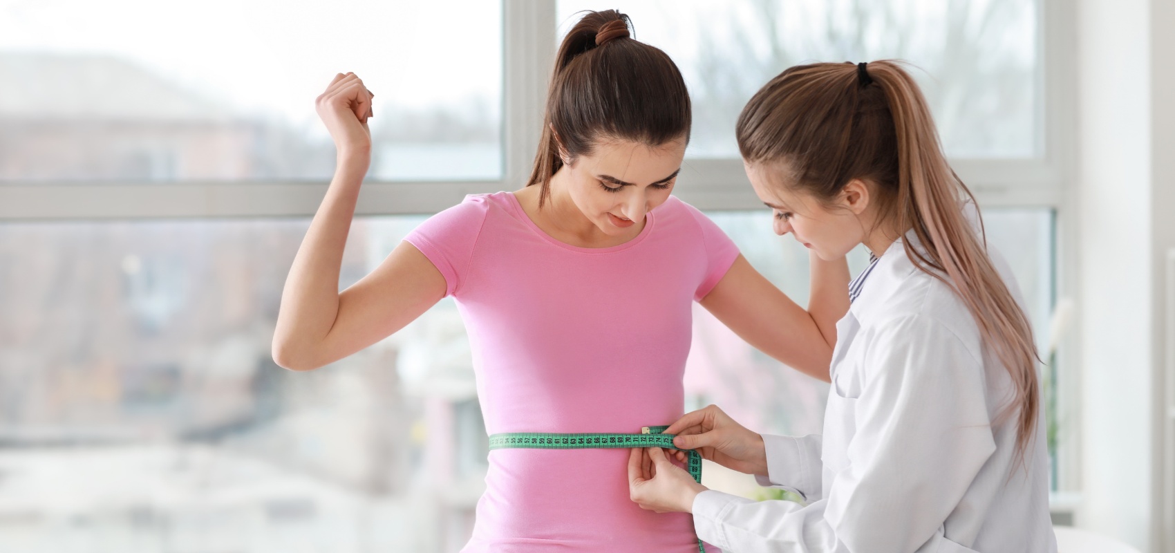 A medical professional measuring the waist of a young woman
