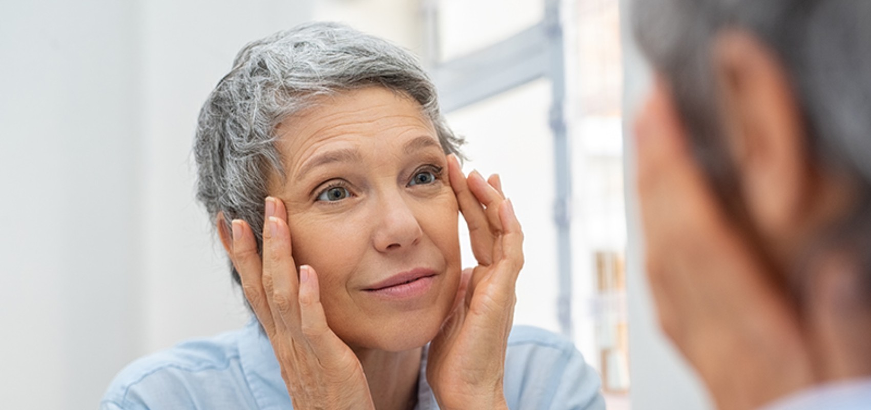 A woman with short grey hair looking into a mirror